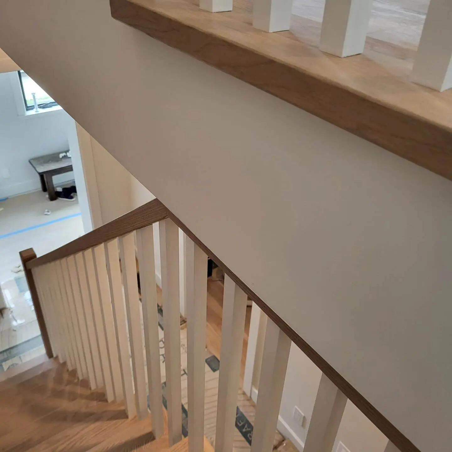Looking down a staircase with wooden treads and white balusters, highlighting the open floor plan below.