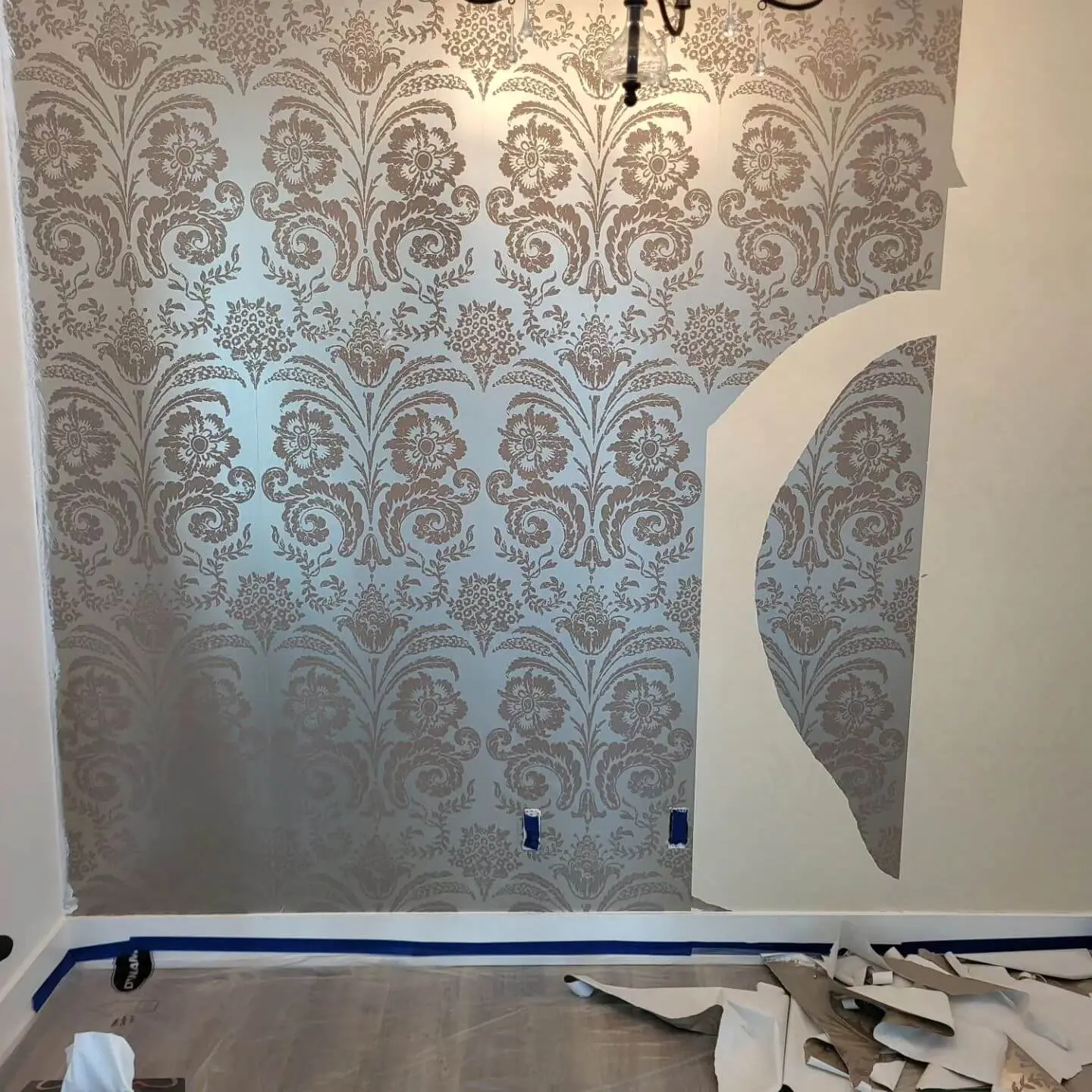 Partially installed decorative wallpaper with an elegant floral damask pattern, highlighting the progress of a wall renovation project.